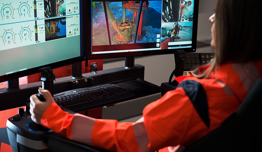 A woman in work clothes sitting at a desk in a control room supervising drilling operations via computer screens. (photo)