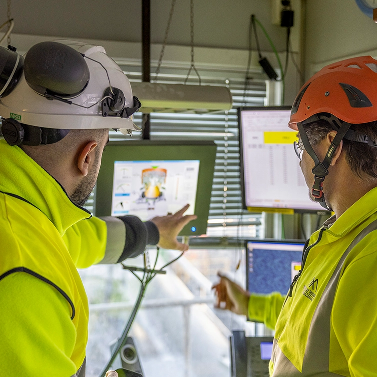 Two persons with helments watching screens (photo)