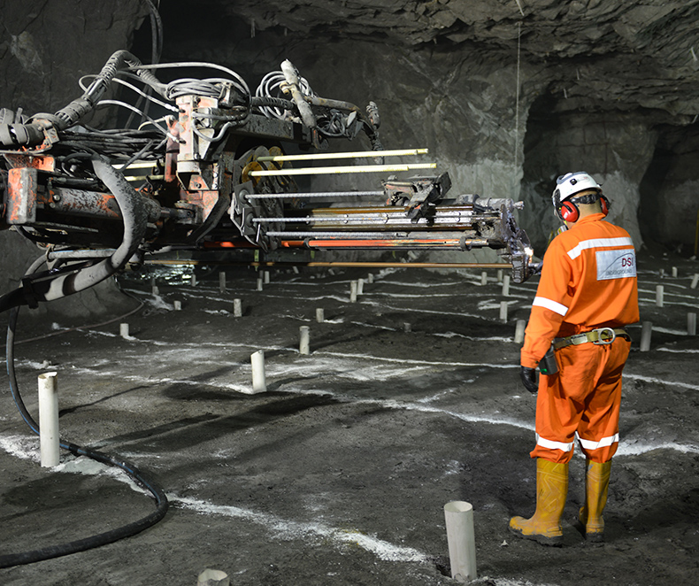 En man i arbetskläder och hjälm som står bredvid utrustning för bergförstärkning i en gruva under jord. (foto)