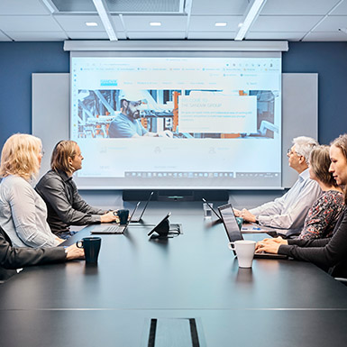 Fem personer som sittar på en stor skärm i ett mötesrum (foto)