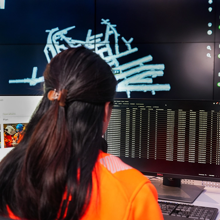 Kvinna sitter framför skärmar I ett kontrollrum (foto)